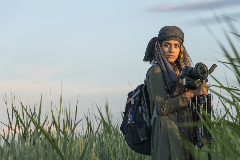 a woman holding a camera in a field of tall grass