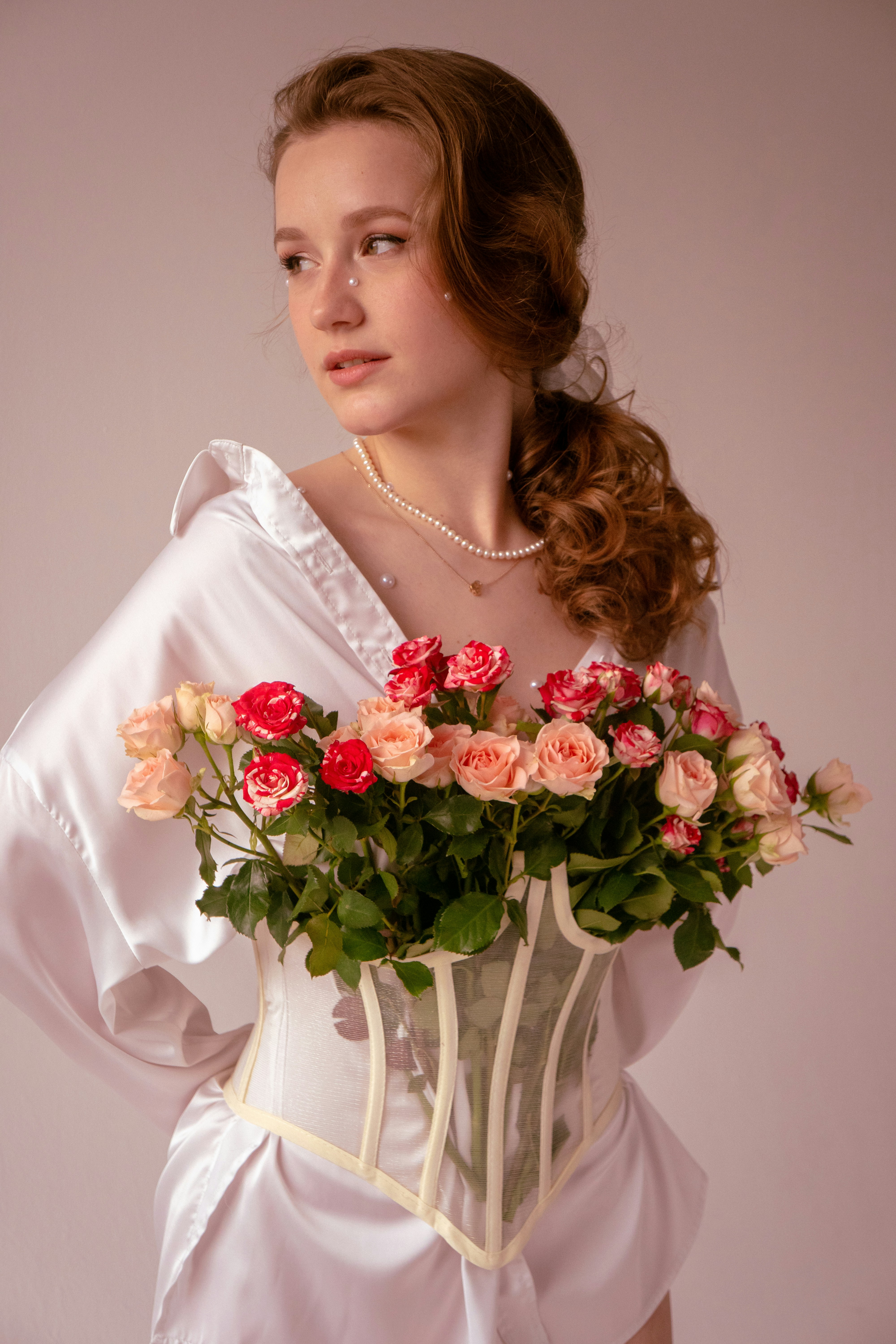 A tender girl in a white shirt in a corset with a bouquet of roses, with a make-up with pearls and a pearl necklace