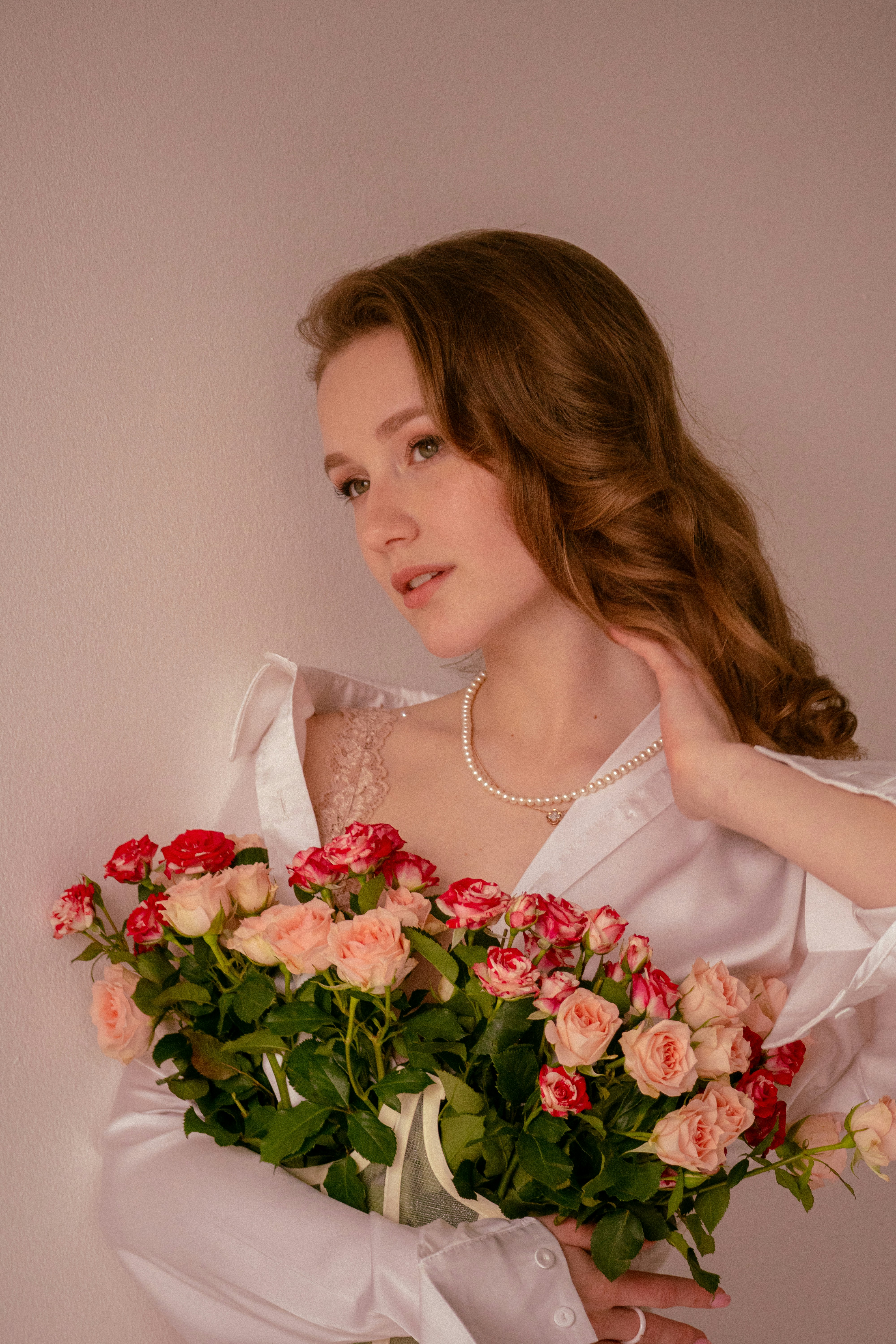 A tender girl in a white shirt in a corset with a bouquet of roses, with a make-up with pearls and a pearl necklace