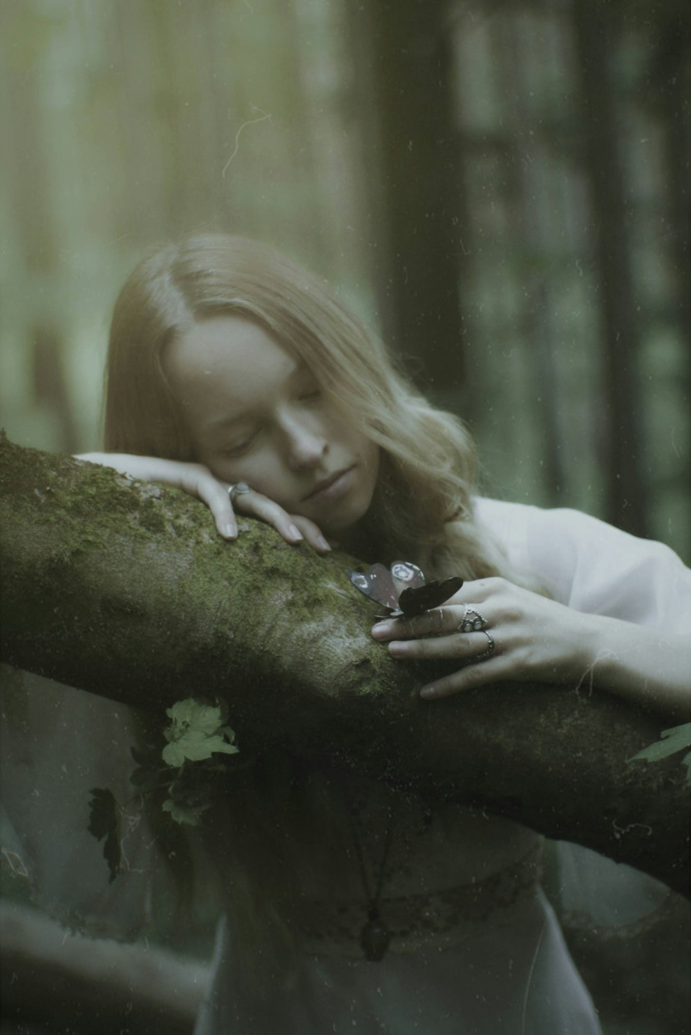 a woman in a white dress leaning on a tree branch