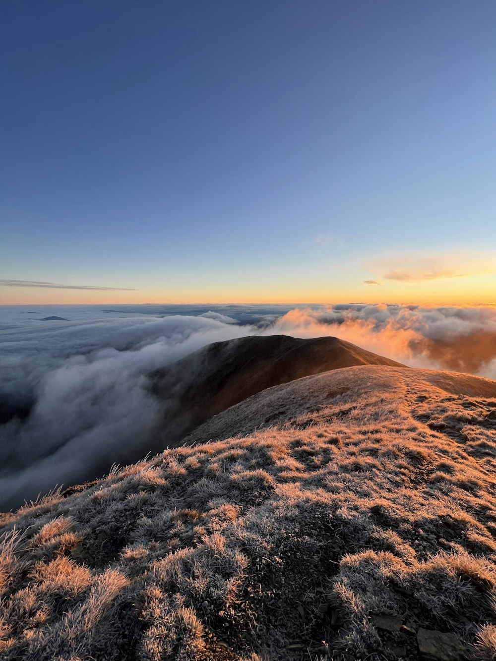 the sun is setting over the clouds on top of a mountain