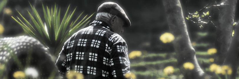 A caring nurse helping an elderly man walk through a sunny garden outside the clinic, with blue accents visible.