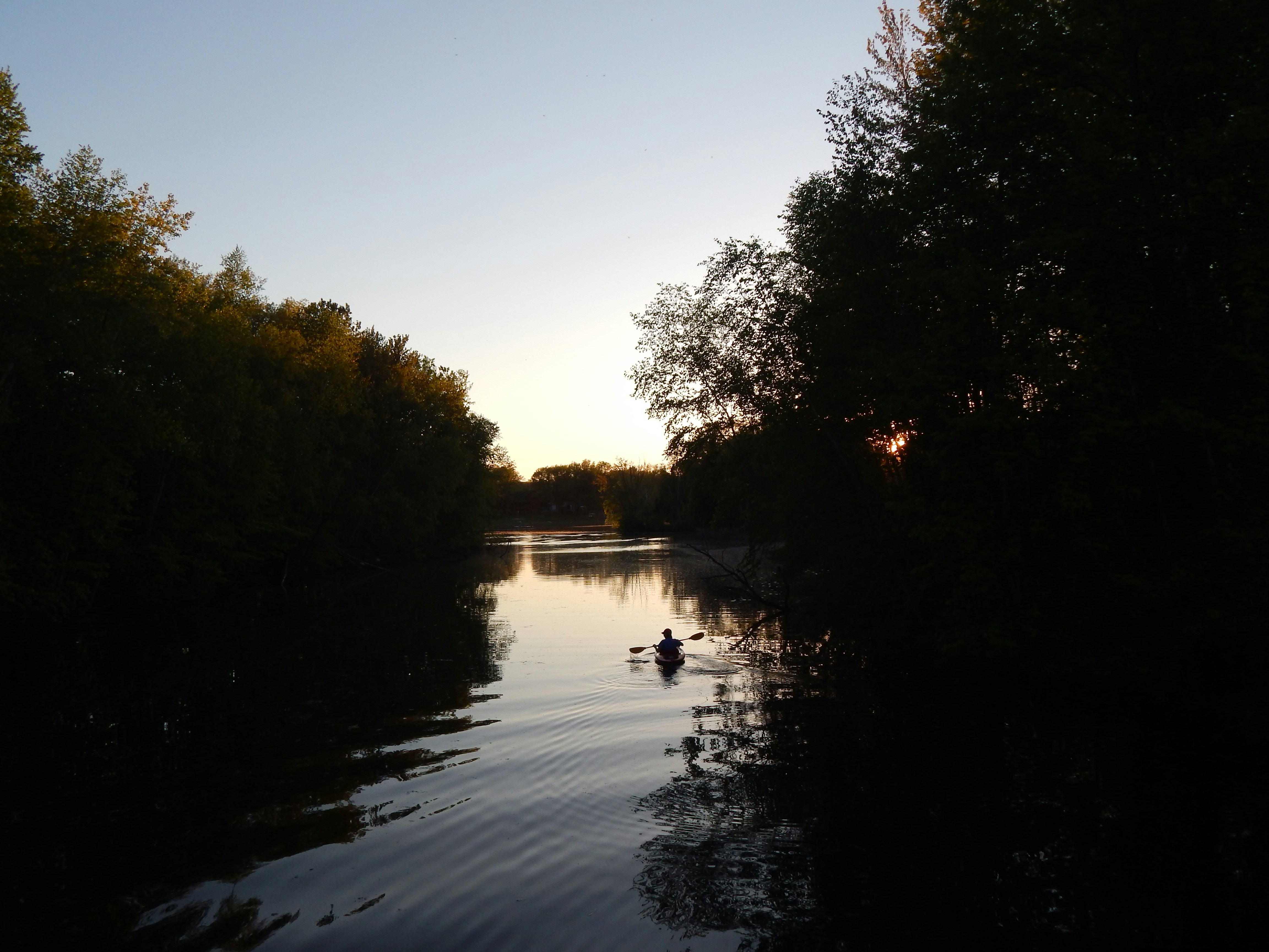 a person paddling a canoe down a river at sunset