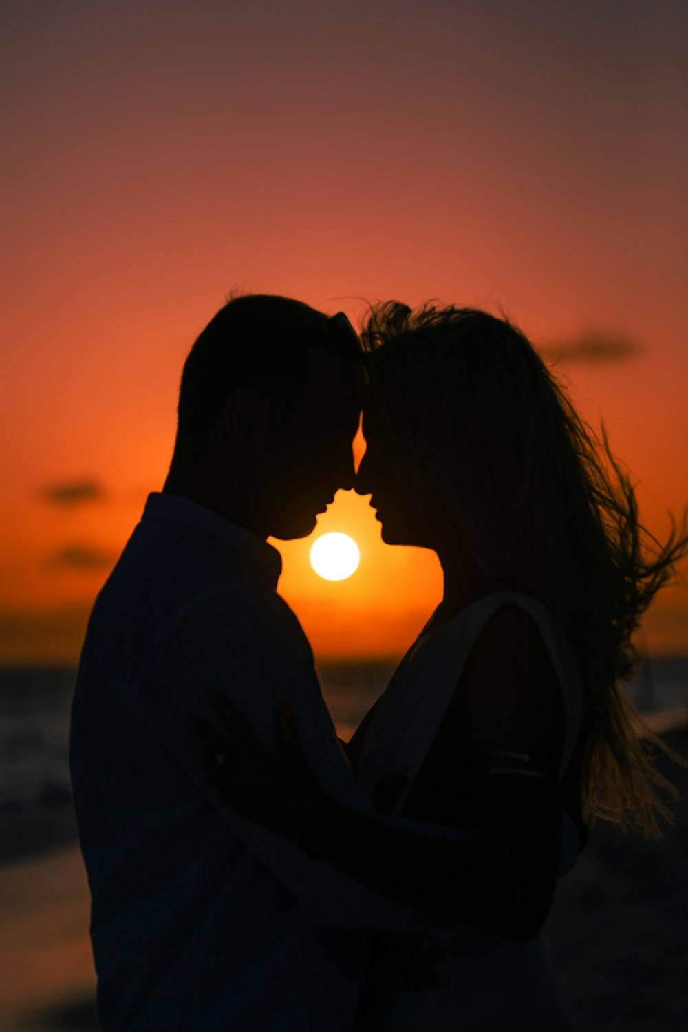 a man and a woman standing next to each other in front of a sunset