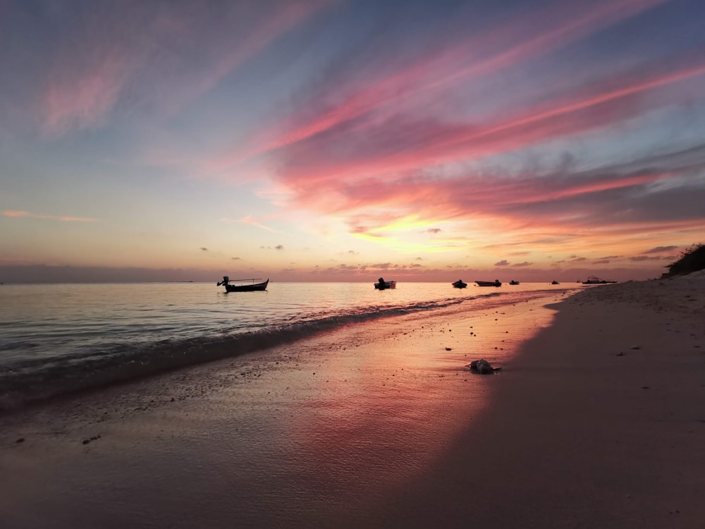 a sunset on a beach with boats in the water