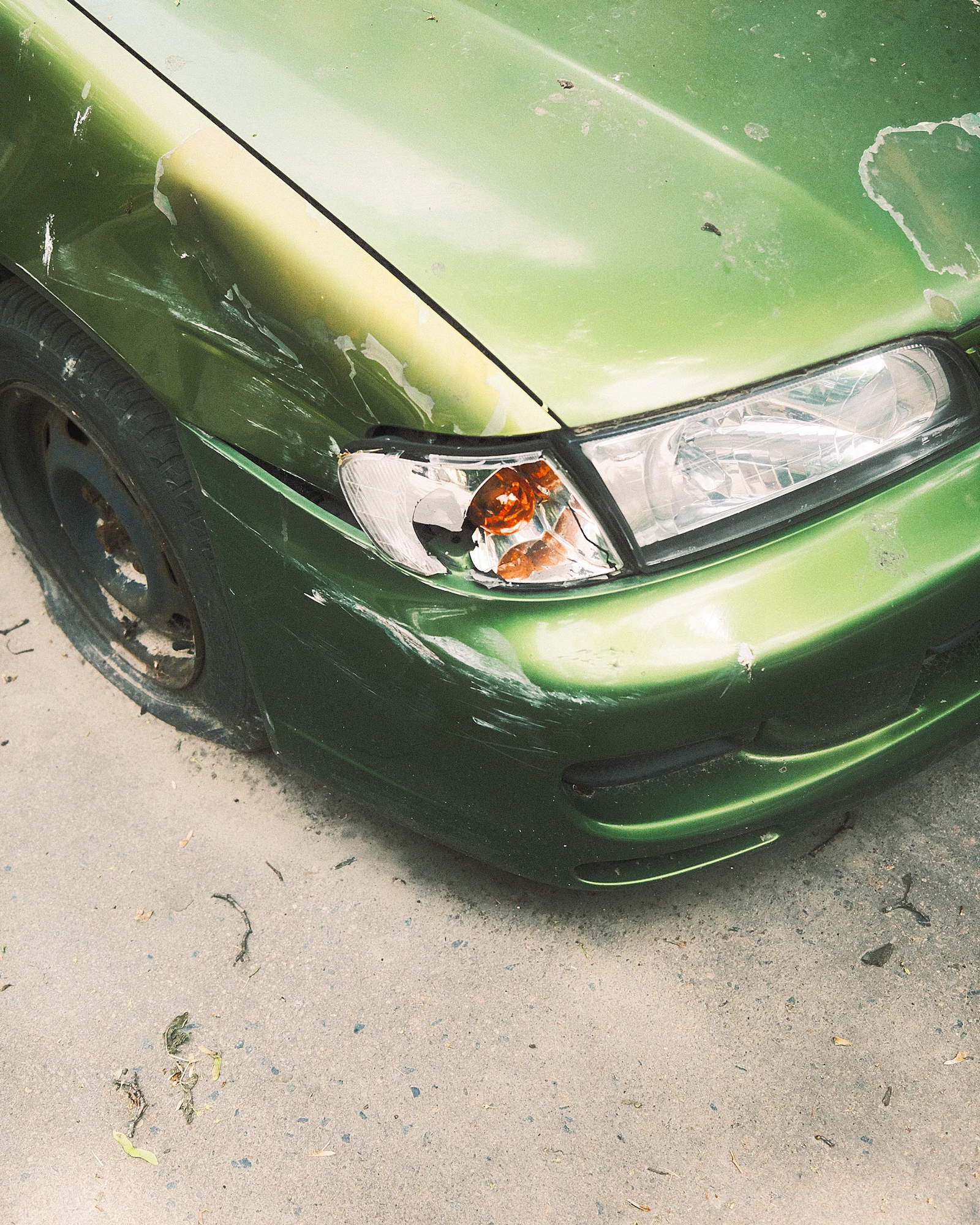 A car's dented front fender and cracked headlight before collision repair