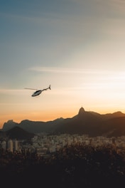 A luxury helicopter hovering above a scenic cityscape during sunset, ready for passengers.