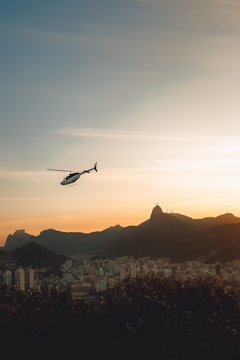 A luxury helicopter hovering above a scenic cityscape during sunset, ready for passengers.