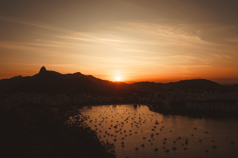 um pôr do sol sobre um corpo de água com uma montanha ao fundo