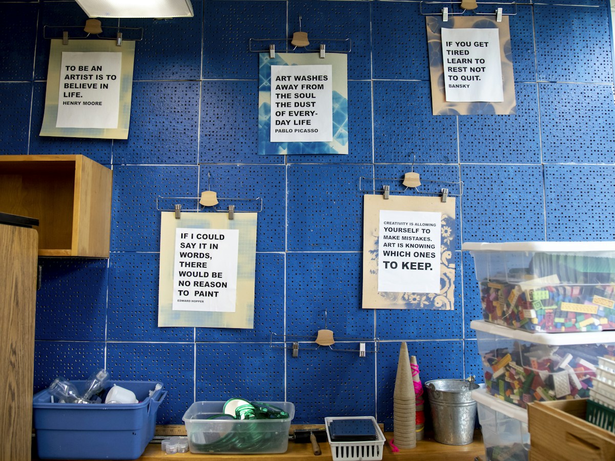 A blue tiled wall with colorful signs displaying various 100th day of school activities and craft ideas.
