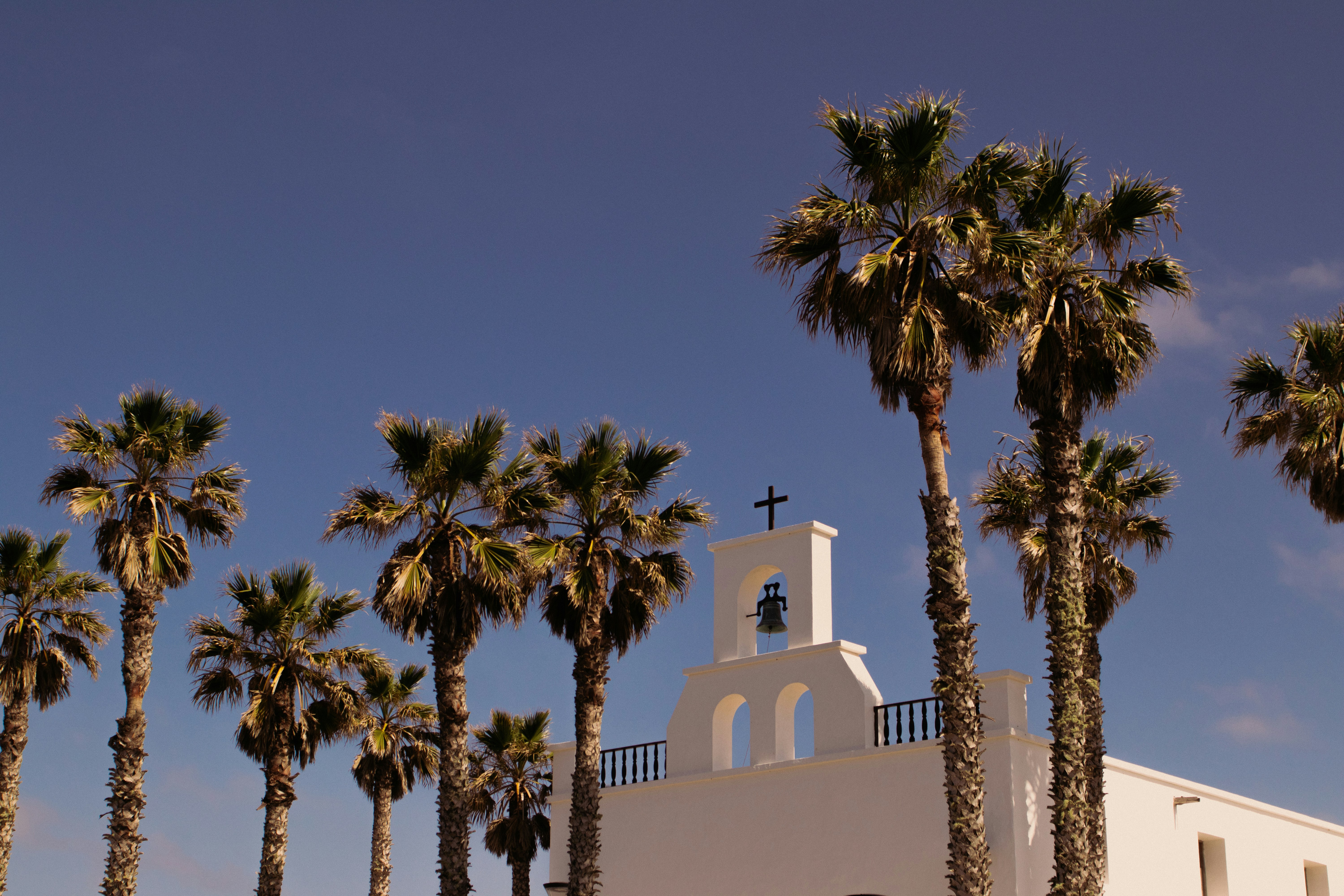 a church with a bell tower surrounded by palm trees, To be in Lanzarote is to wonder if you are in Mexico, Costa Rica or scattered on a volcanic island in the ocean.