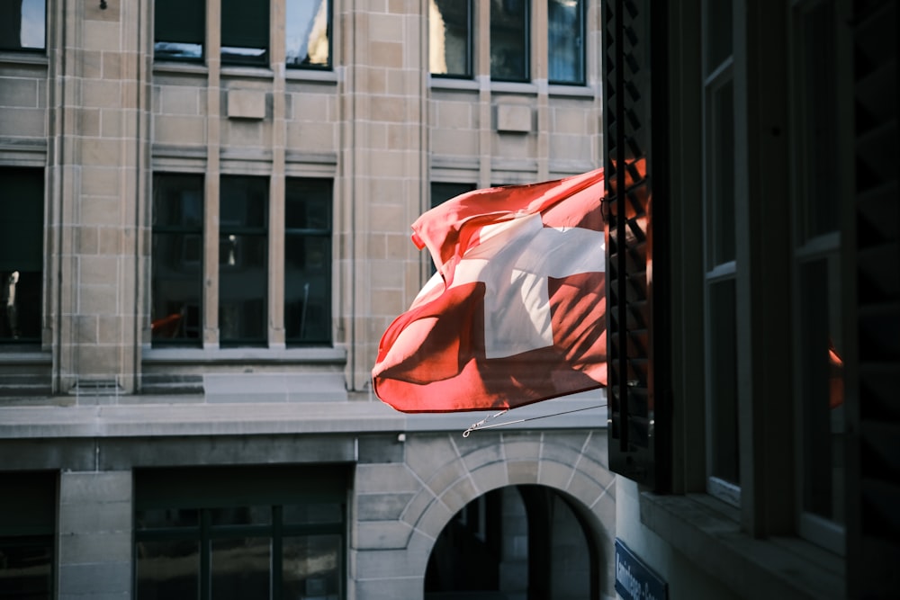 a red and white flag flying in front of a building