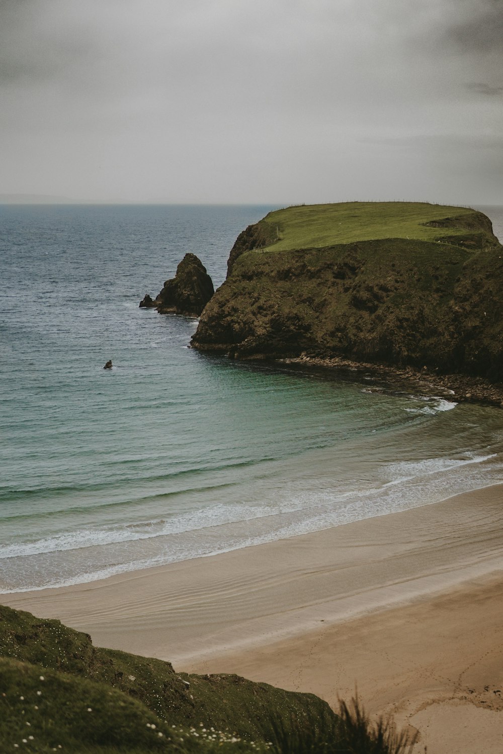 a sandy beach next to the ocean under a cloudy sky