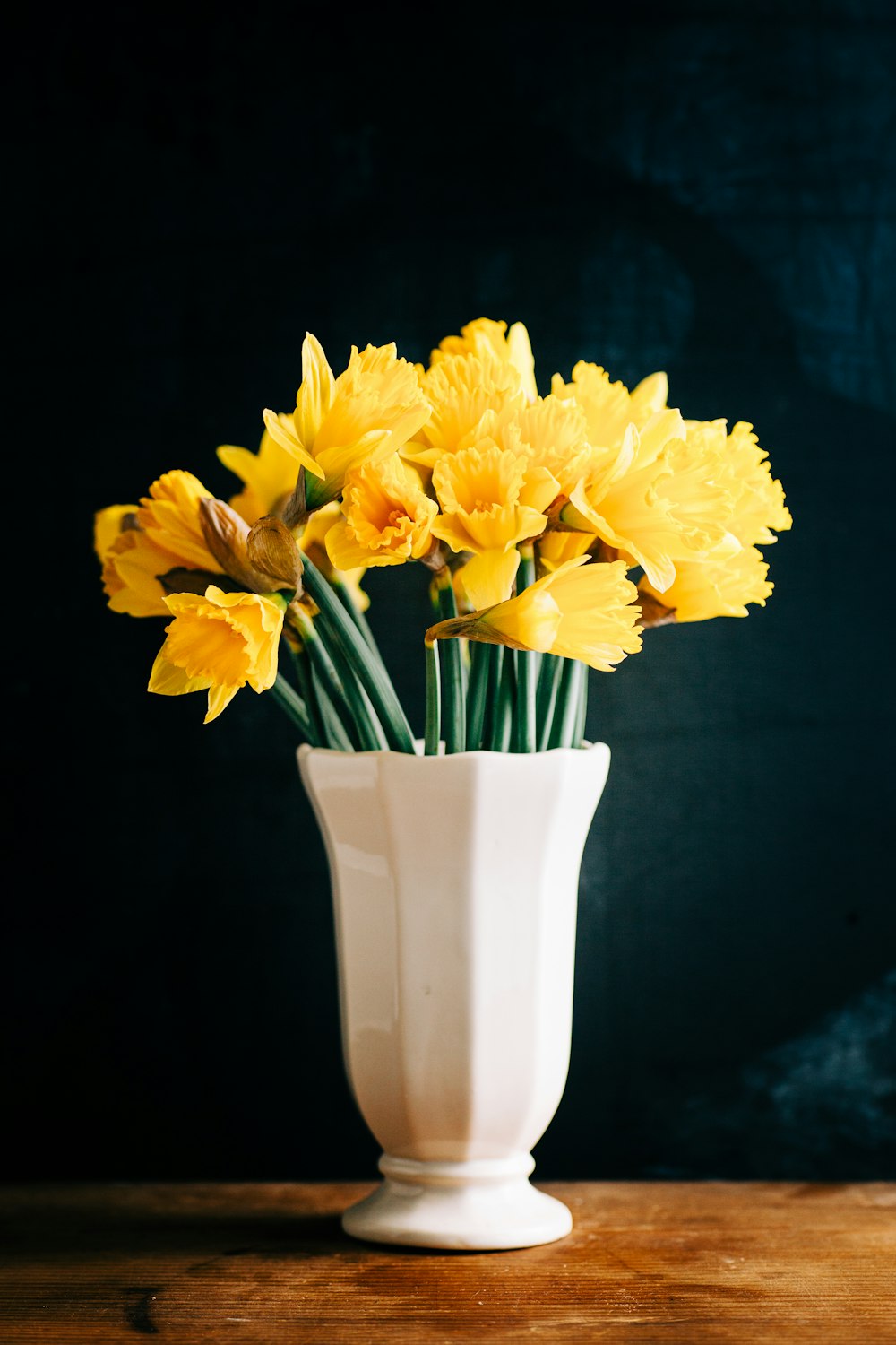 a white vase filled with yellow flowers on top of a table