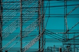 An intricate metal scaffolding structure composed of multiple intersecting bars and beams with a clear blue sky as the background.