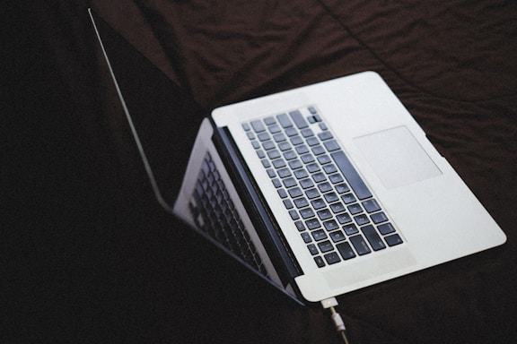A laptop partially open, viewed from an angle showing the keyboard and part of the screen, resting on a dark surface.