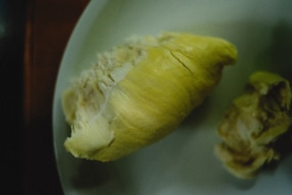 A piece of durian with its yellow, fleshy interior exposed, placed on a white plate.