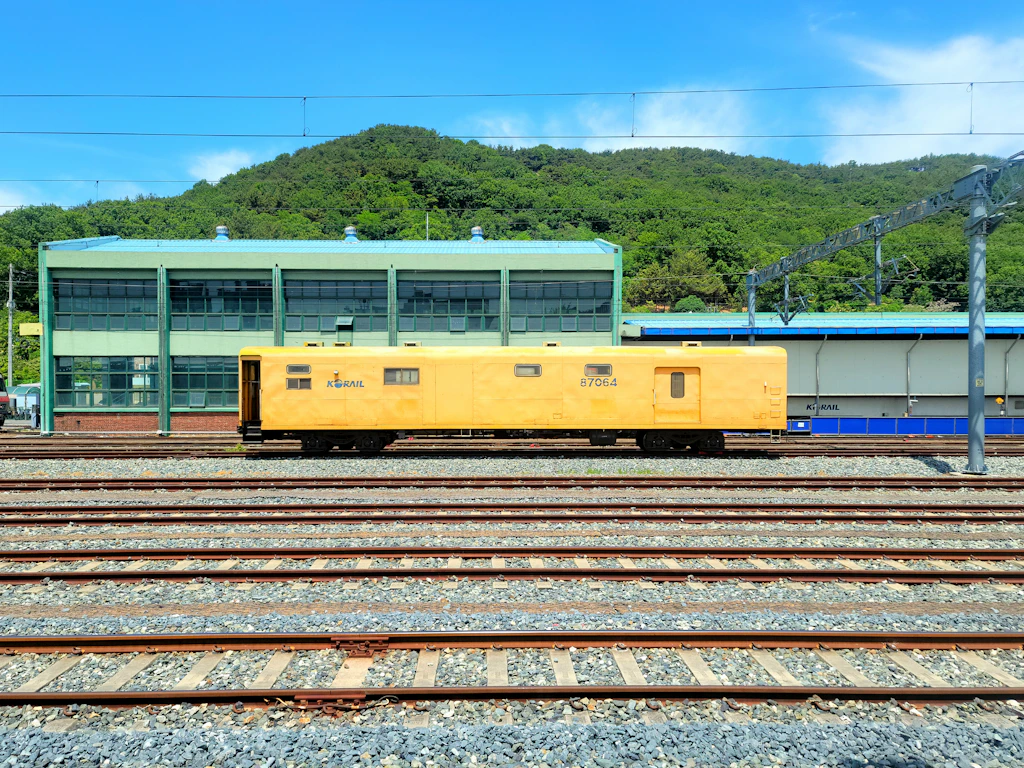 Yellow track maintenance vehicle on railway tracks in a rail yard, with an industrial building behind