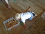 A child in soft brown clothing playing with a wooden train set on a cream floor.