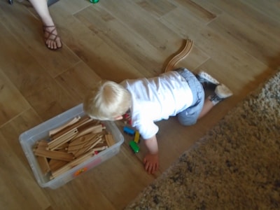 A child in soft brown clothing playing with a wooden train set on a cream floor.