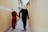 A couple wearing traditional Vietnamese clothing walks hand in hand down a narrow, yellow-walled alley. Both are sporting conical hats known as non la. The woman is dressed in a red ao dai, while the man wears a black one.