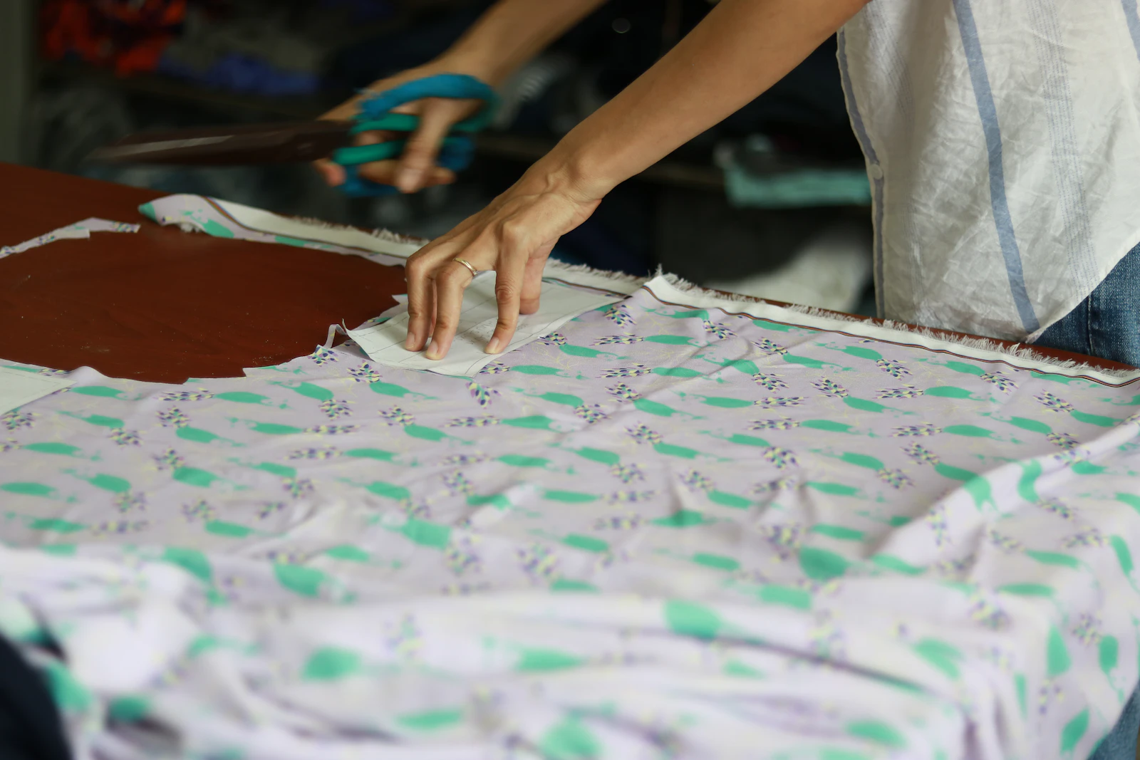 Close-up of a tailor cutting fabric with shears on a cutting table during womenswear garment production