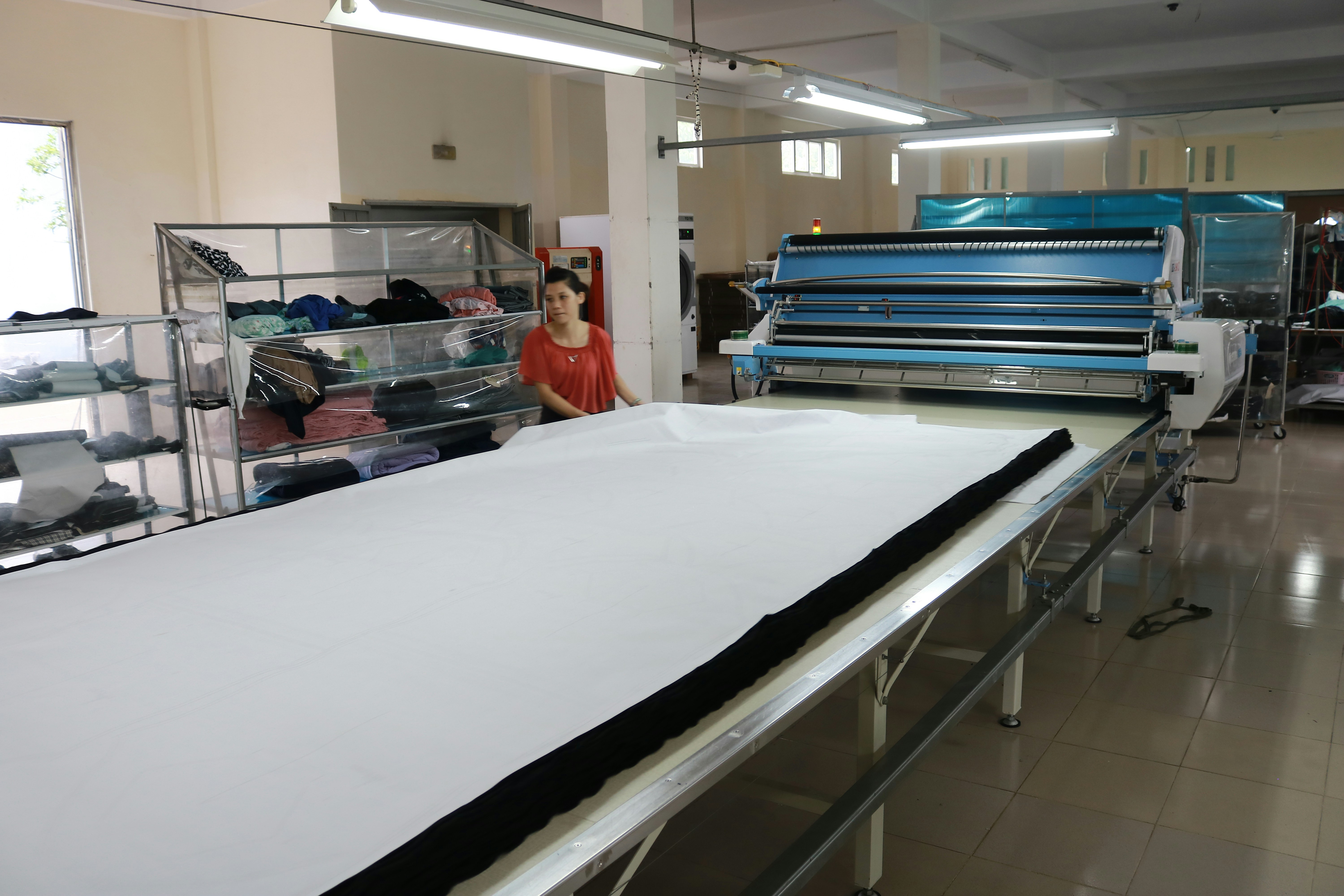 Industrial fabric cutting with large cutting machine, colorful fabric rolls in background, manufacturing floor