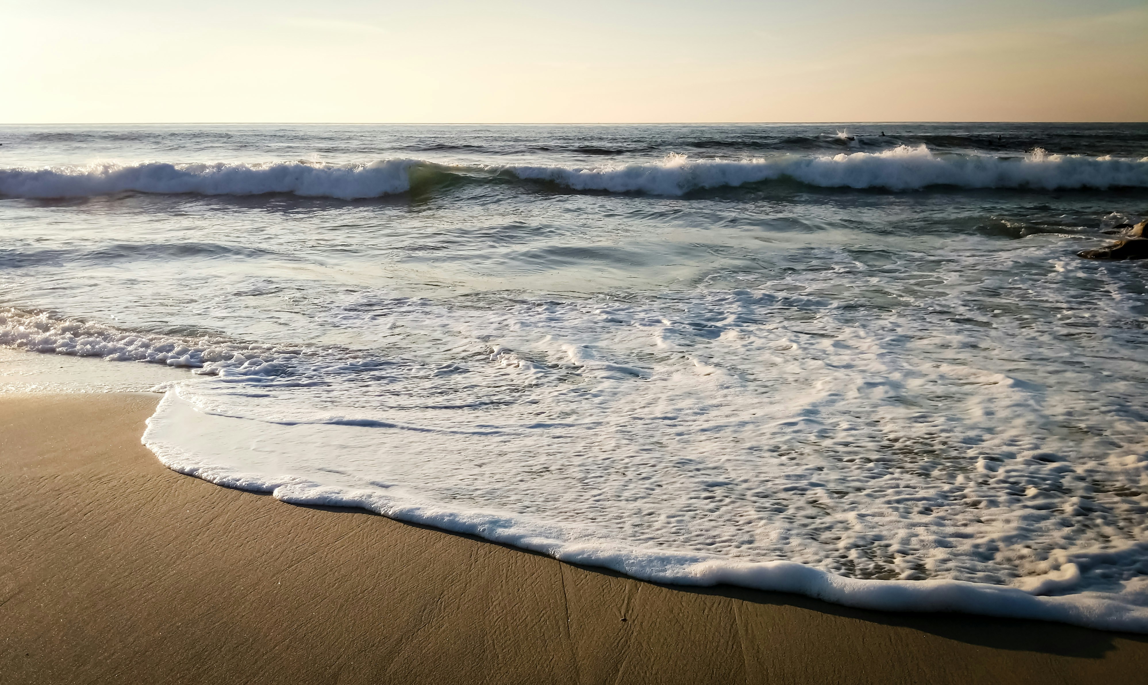 a sandy beach with waves coming in and out of the water, Waves crashing.