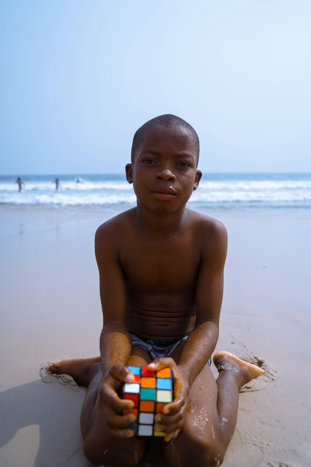 a young boy sitting on a beach holding a rubik cube