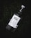 A bottle of Ojo de Tigre Mezcal lies on grass. The bottle has a white label with detailed information including the type and origin of the mezcal. The cap is secured with a metal clasp.