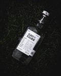 A bottle of Ojo de Tigre Mezcal lies on grass. The bottle has a white label with detailed information including the type and origin of the mezcal. The cap is secured with a metal clasp.