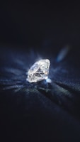 A brilliant cut diamond sits elegantly on a dark surface, reflecting light and casting a delicate play of shadows and sparkles around it.