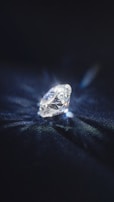 A brilliant cut diamond sits elegantly on a dark surface, reflecting light and casting a delicate play of shadows and sparkles around it.
