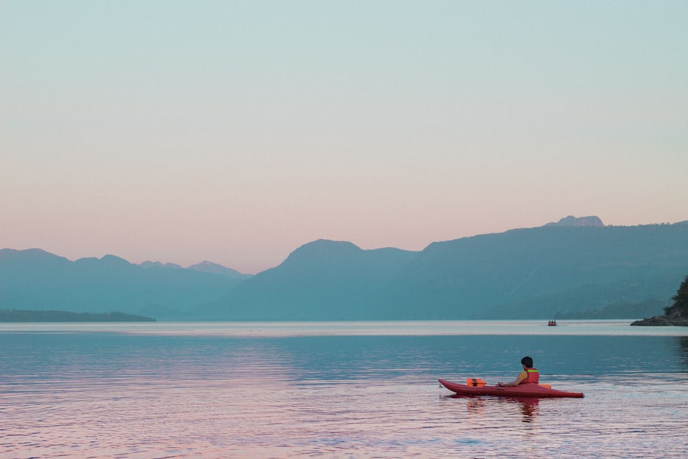 a person in a kayak on a lake with mountains in the background