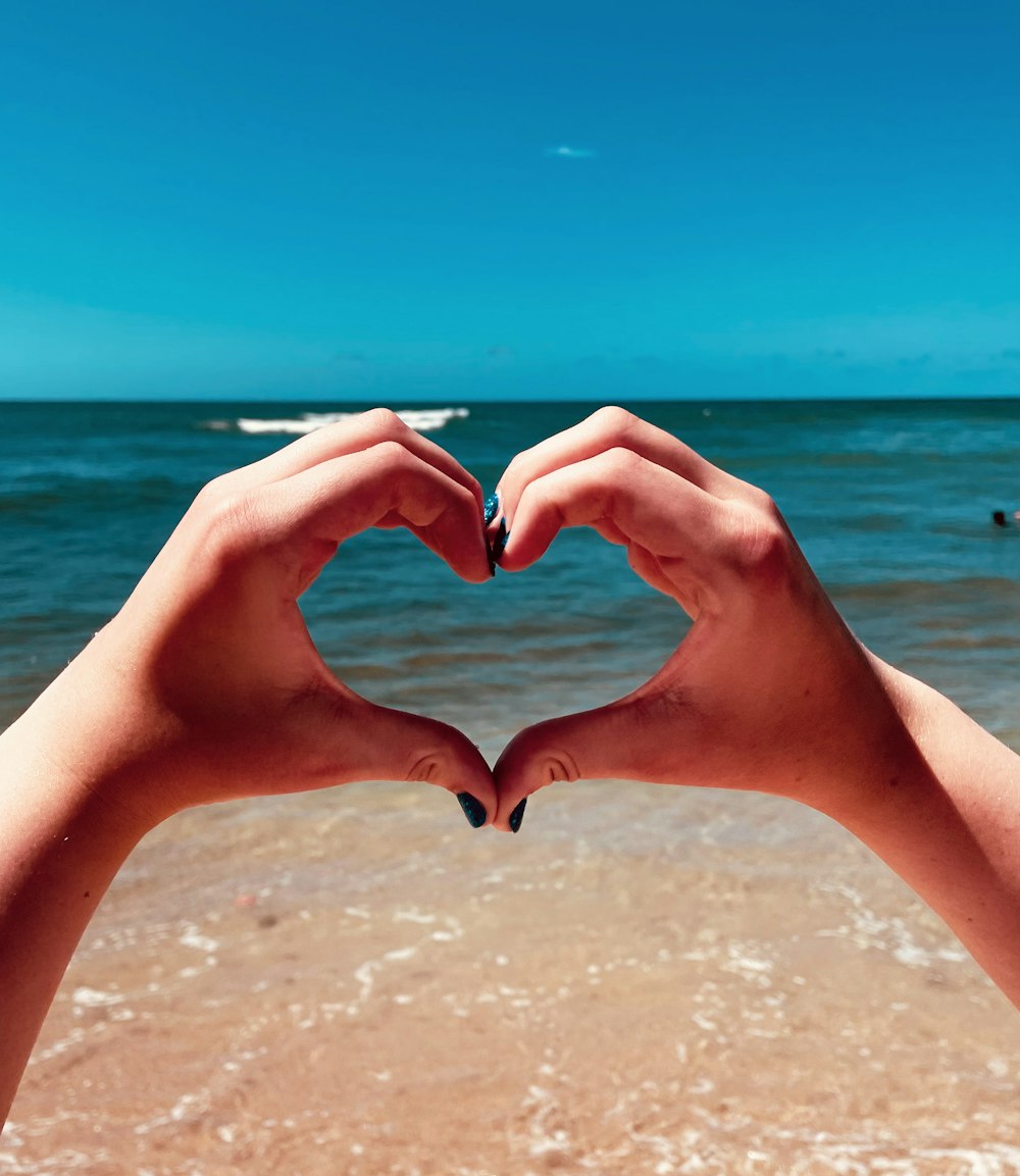 two hands making a heart shape on a beach