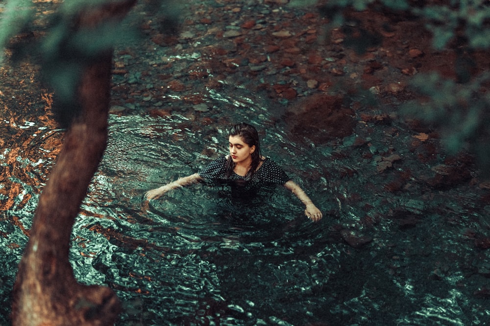 a woman swimming in a pool of water next to a tree