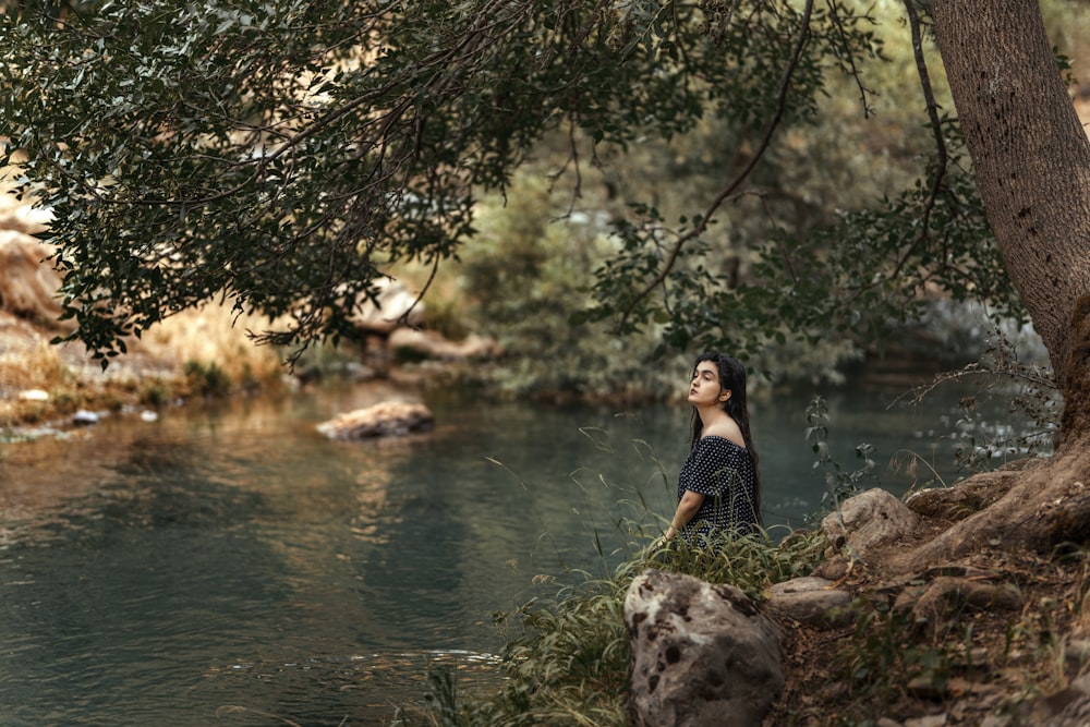 a woman in a black dress standing on a rock next to a river