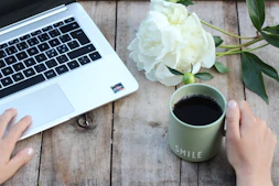 A friendly person typing on a laptop with coffee beside them, symbolizing reaching out.