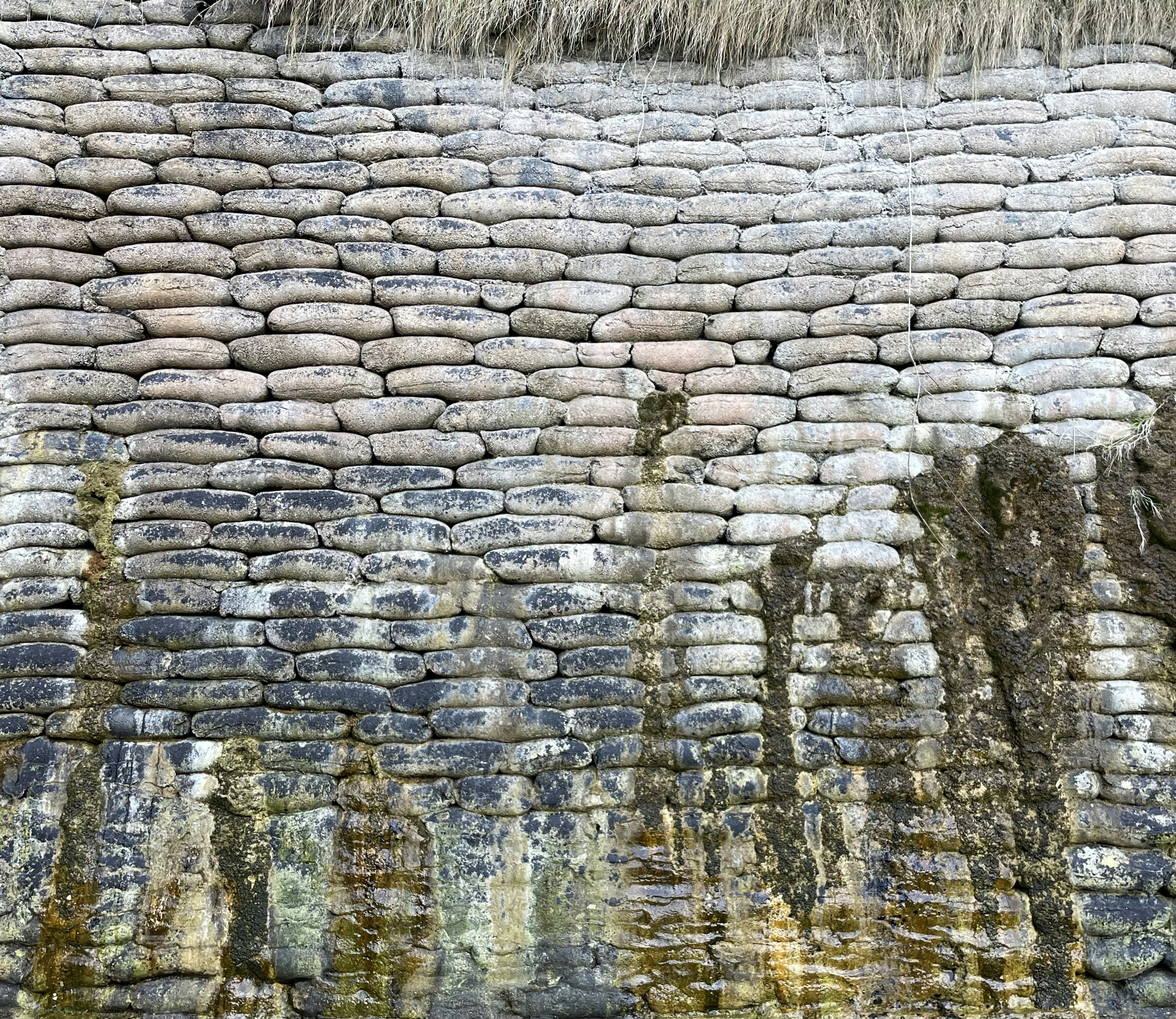 Sand bags stacked to create a supporting wall against a rocky cliff on the beach. 