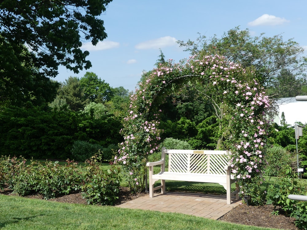 a white bench sitting in a garden next to a lush green field