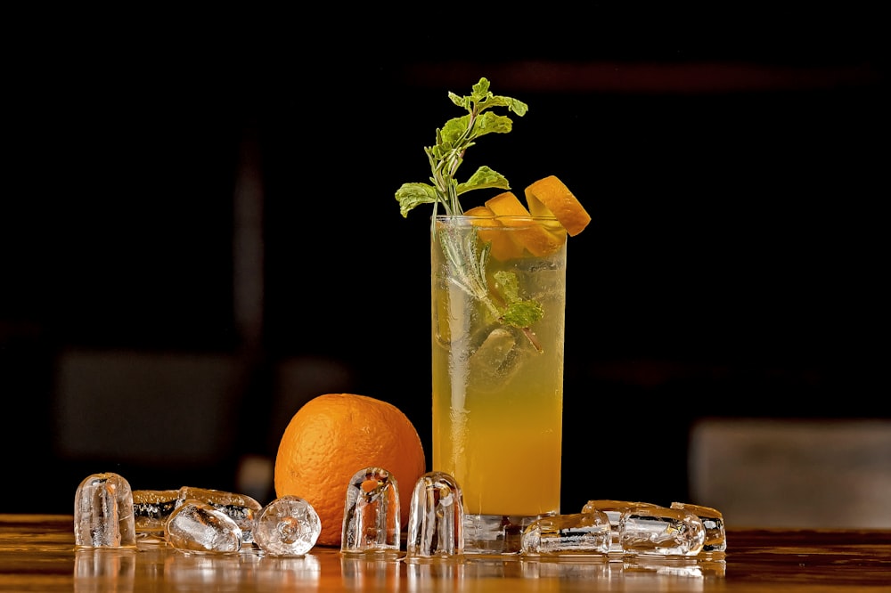 a tall glass filled with a drink next to an orange