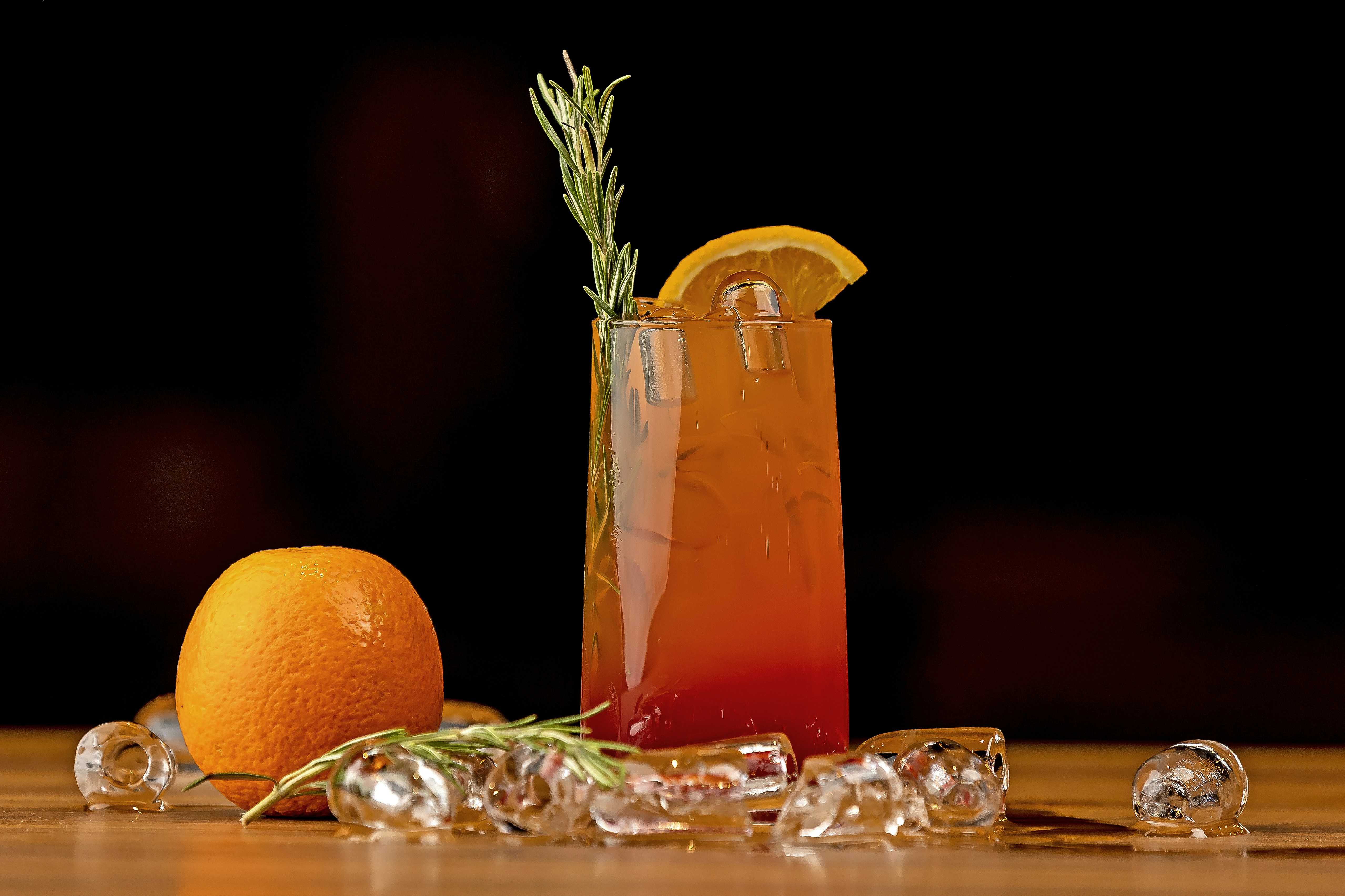 a glass of orange juice next to an orange and a rosemary garnish