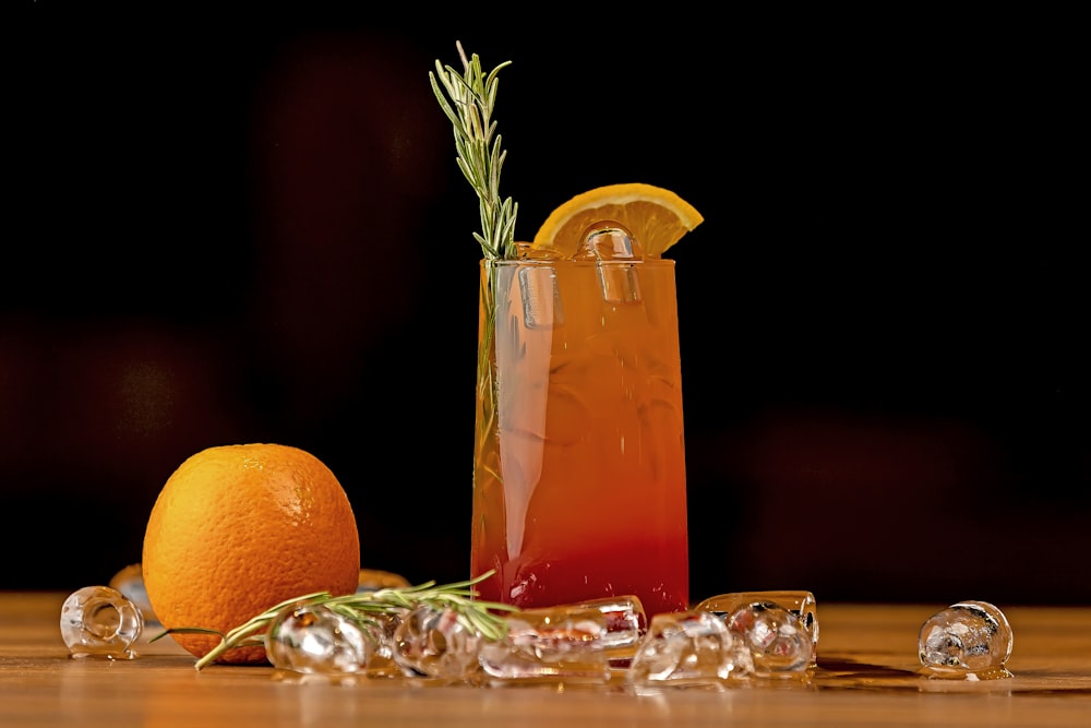 a glass of orange juice next to an orange and a rosemary garnish