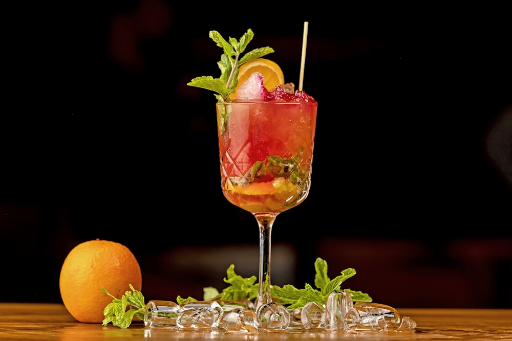 a glass filled with a drink next to an orange