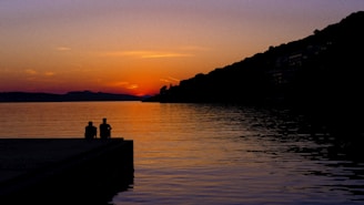 A peaceful travel scene with a couple watching the sunset over a calm lake.