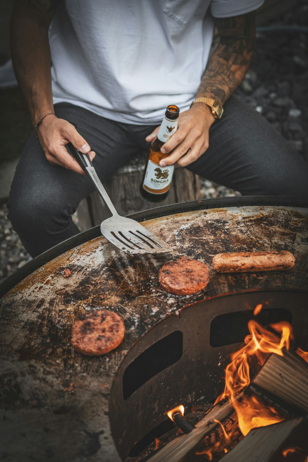 a man holding a bottle of beer over a grill