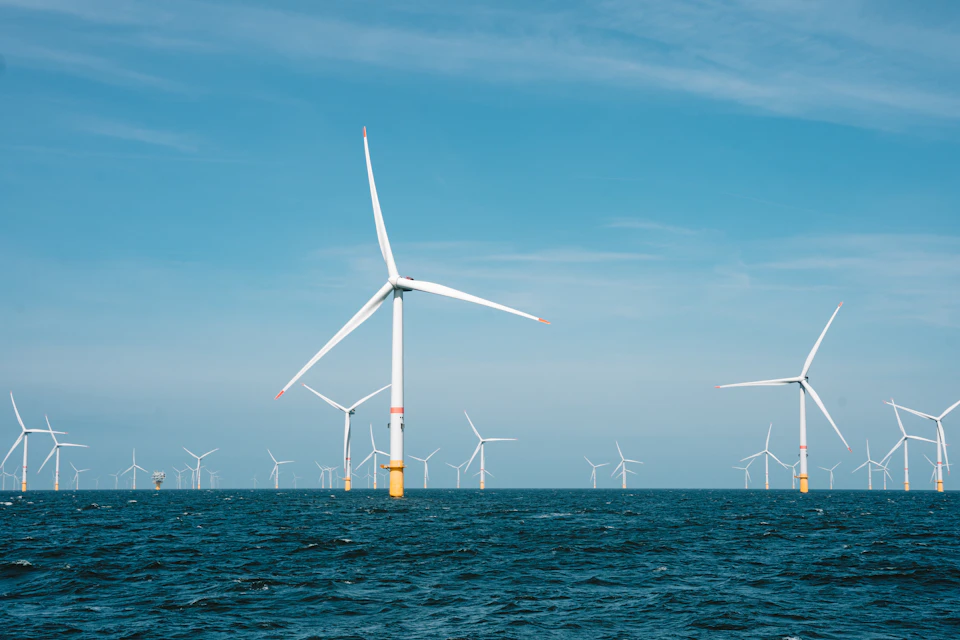 Six wind turbines stand on calm ocean waters, surrounded by white blades and bright colors