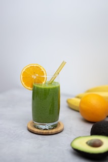 a green smoothie with an orange slice and a straw