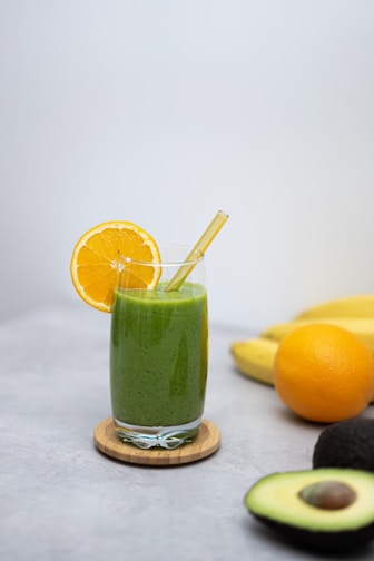 a green smoothie with an orange slice and a straw