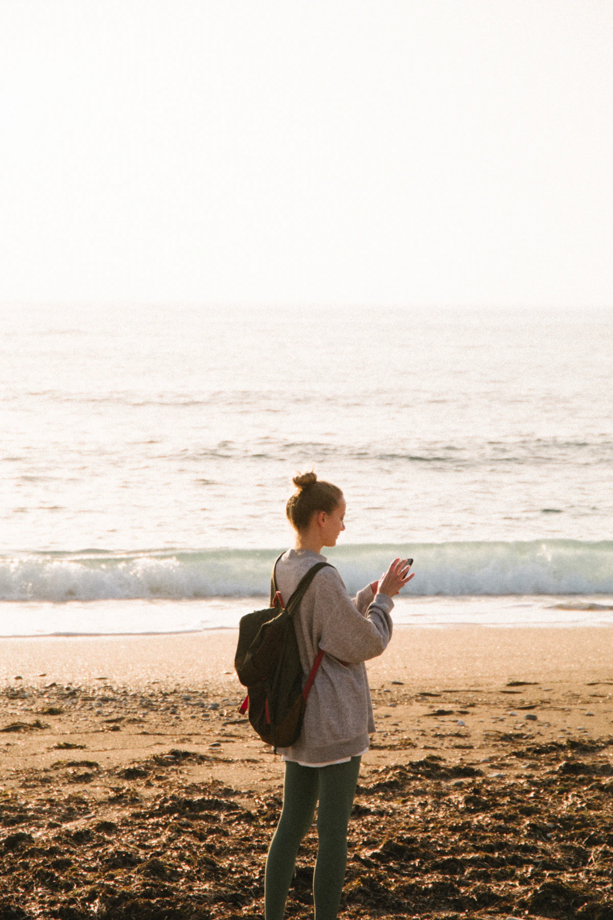 A woman standing on a beach looking down at her phone, the mind still partly at work while on holiday